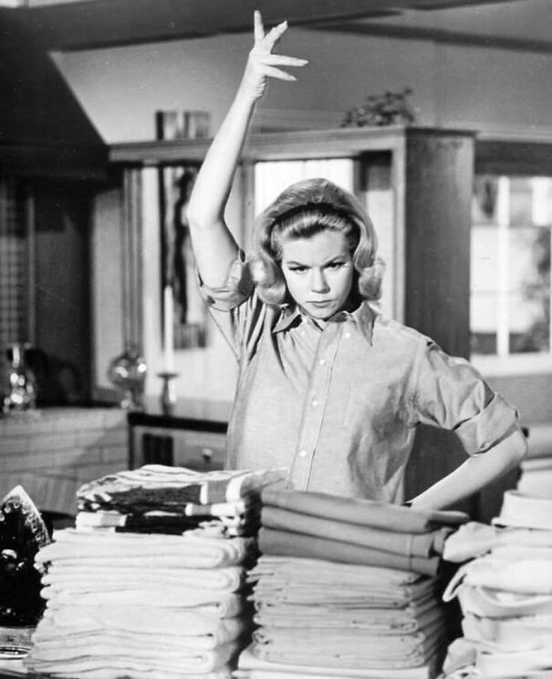 Woman doing housework with a dramatic gesture, evoking a historical perspective of domestic life.