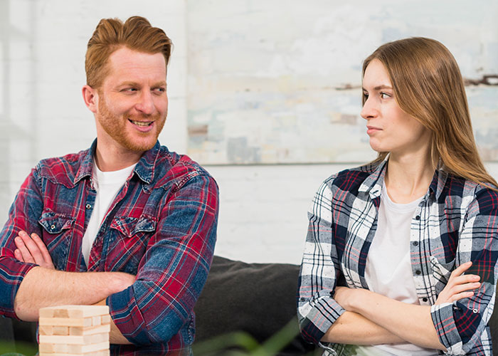 Two people wearing plaid shirts sitting opposite each other with crossed arms, sharing reactions to coming out.