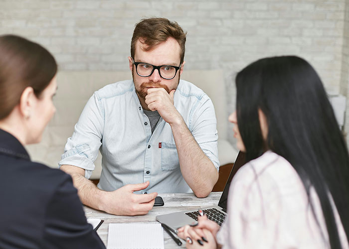 Three people in a discussion around a laptop, potentially highlighting signs of a toxic workplace environment.