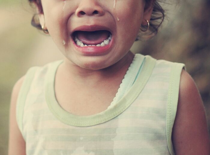 A crying child, tears streaming, wearing a striped tank top.