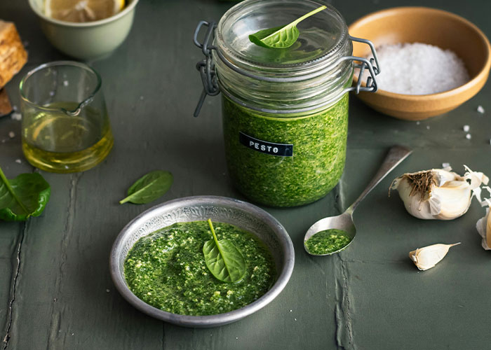 Jar and bowl of pesto sauce with garlic and olive oil on a rustic table.