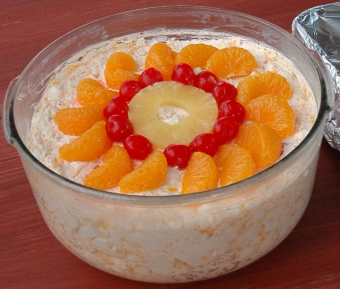 Glass bowl of Watergate Salad topped with pineapple, cherries, and orange slices.
