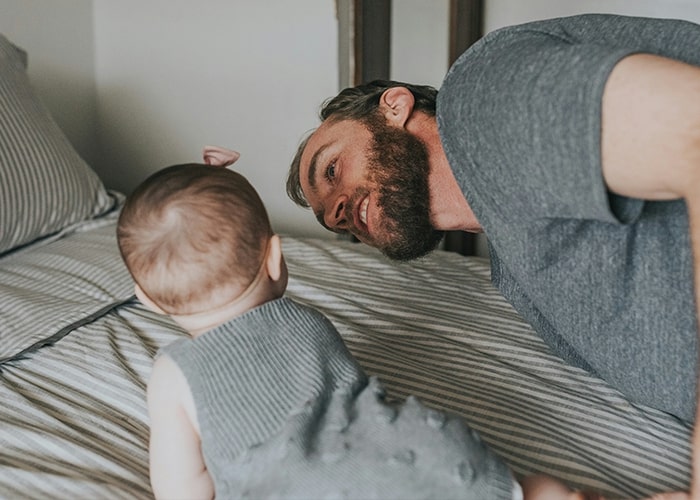 A dad and baby on a bed, engaging playfully, illustrating common parenting mistakes in communication.
