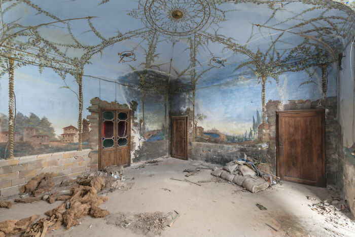 Abandoned room with intricate ceiling design and peeling mural walls, evoking a stunning and eerie atmosphere.