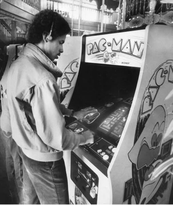 Man playing a vintage Pac-Man arcade game in a historical photo.