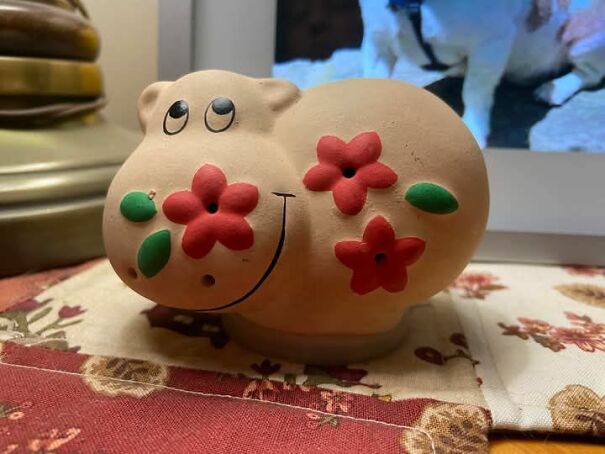 A strange, smiling hippo sculpture adorned with red flowers, found while thrifting.