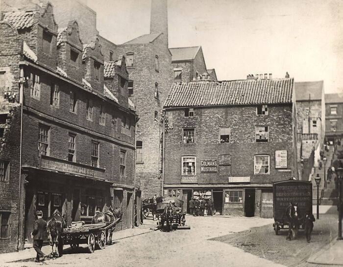 Historic street scene from 50-100 years ago, with horse-drawn carts and brick buildings, showing world change over time.