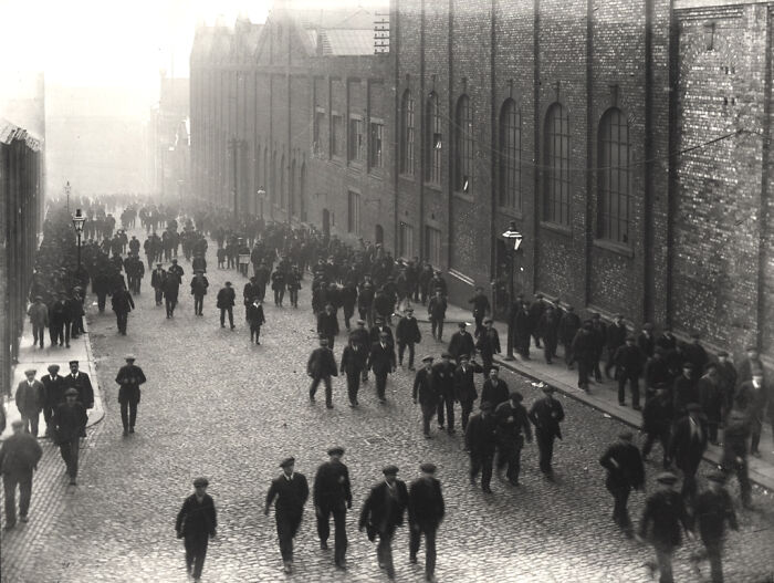 Workers on a cobblestone street outside a factory, showcasing rare historical scenes from 50-100 years ago.