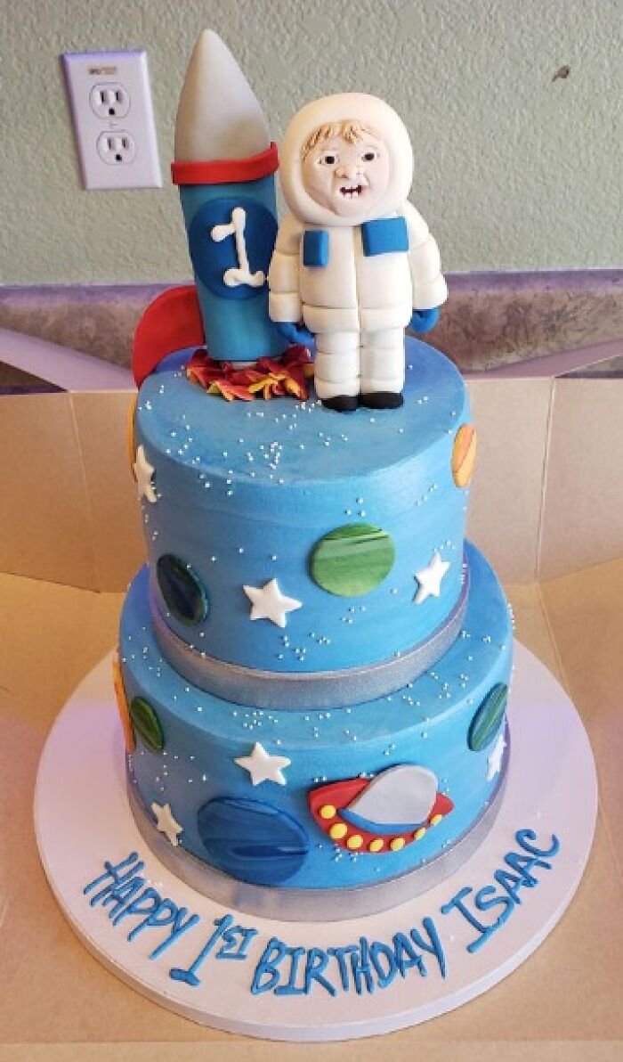 Blue space-themed cake with rocket and astronaut topper, showcasing a funny baking fail.