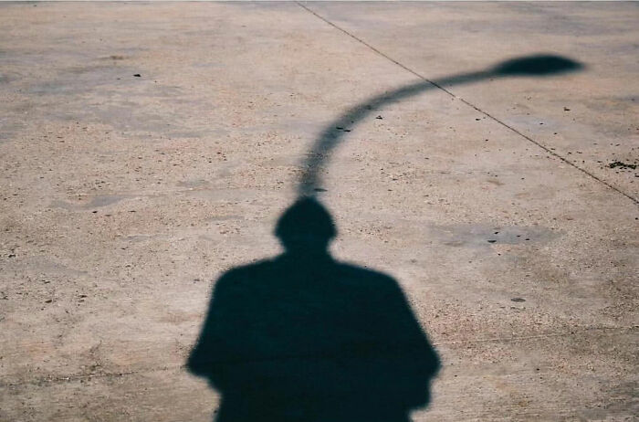 Shadow of a person on concrete, blending with a streetlamp, highlighting the raw beauty of street life photography.