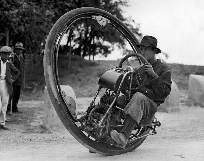 Man riding a monocycle, a weird invention once seen as revolutionary, observed by onlookers.