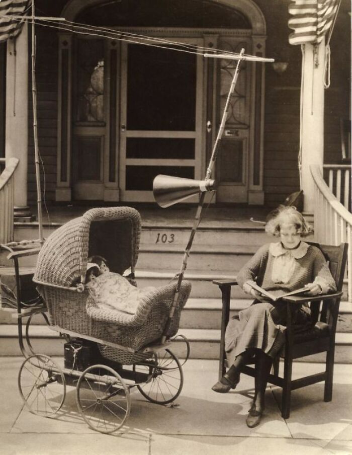 Vintage invention: 1920s baby pram with radio antenna, woman reading beside it.