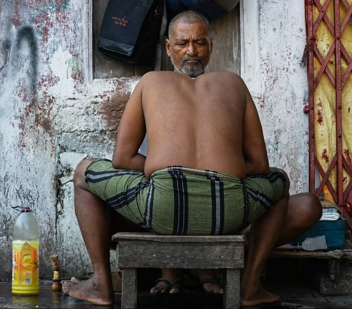 Man sitting on a stool in a street scene, wearing striped shorts, creating an unexpected moment.