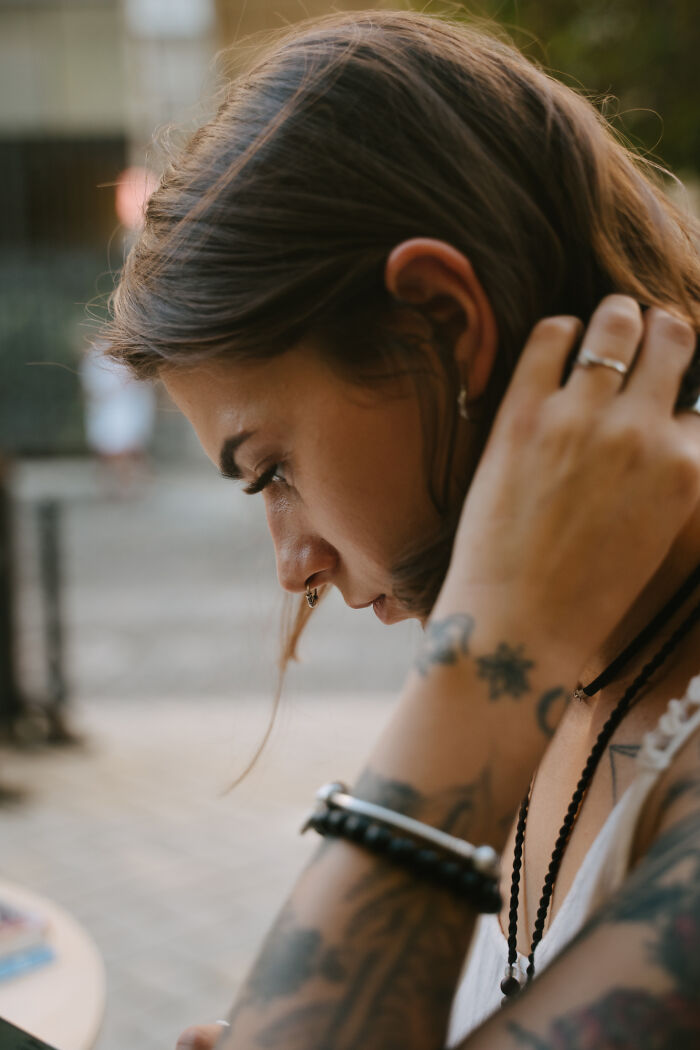 Young woman with tattoos adjusts hair, pondering perceptions of normalcy.
