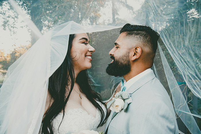 Bride and groom smiling under a veil, highlighting wedding red flags discussion. Bride and groom smiling under a veil, highlighting wedding red flags discussion.