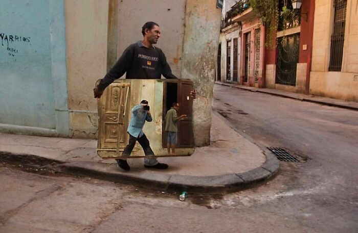 Man carrying a large mirror on a street, perfectly timed to reflect a parallel scene.
