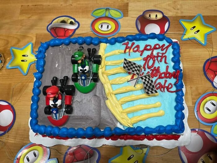 Funny baking fail cake with racing theme and toy cars, decorated with colorful icing and birthday message.