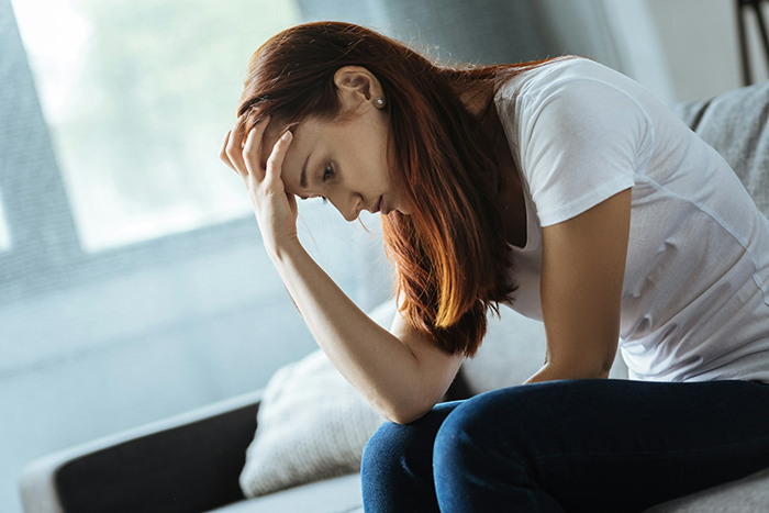 A worried woman sitting on a sofa, considering advice on friend's wedding red flags, hand on forehead. A worried woman sitting on a sofa, considering advice on friend's wedding red flags, hand on forehead.