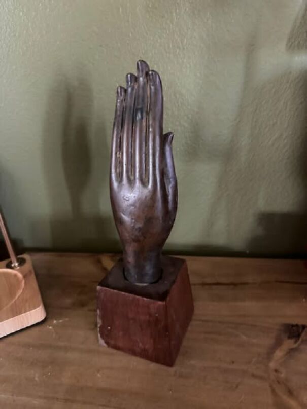 Strange thrifting find: a metal hand sculpture on a wooden base displayed on a table.