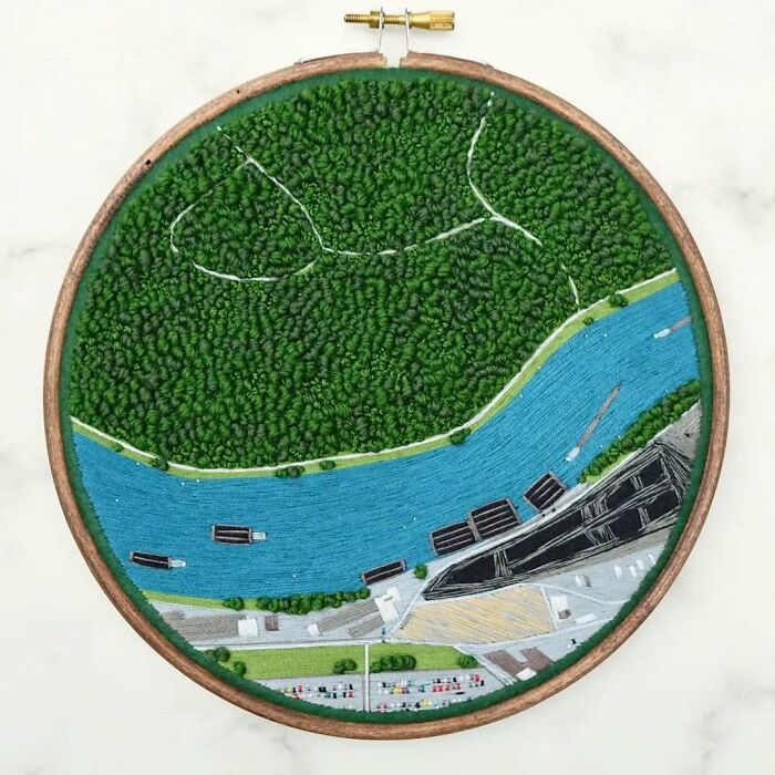 Embroidery of a lush landscape with a river and structures, showcasing incredible craftsmanship.