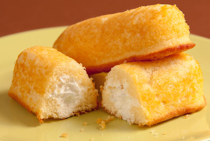 Three creamy sponge cakes on a yellow plate, a food some find unappealing despite its global popularity.