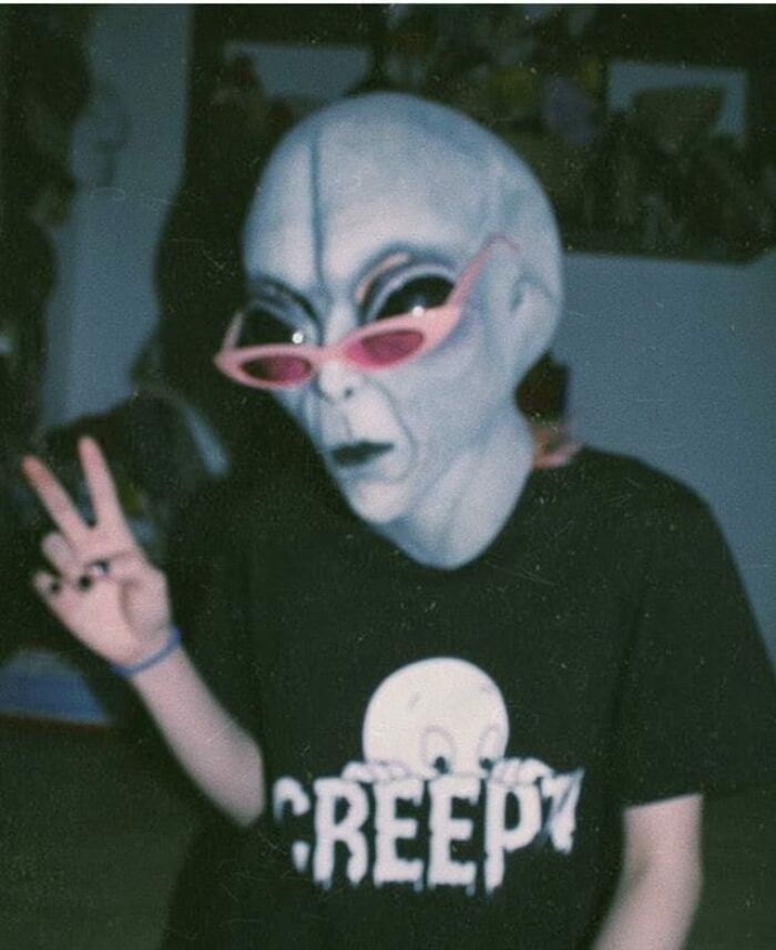 Alien mask, pink sunglasses, "Creepy" shirt, peace sign; funny random photo.