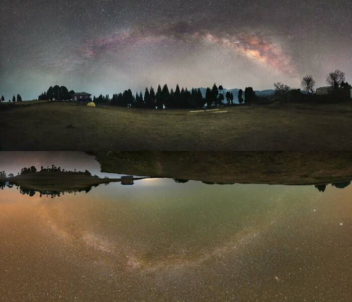 Astrophotography: Stunning Milky Way arc over a serene landscape reflected in a tranquil body of water.