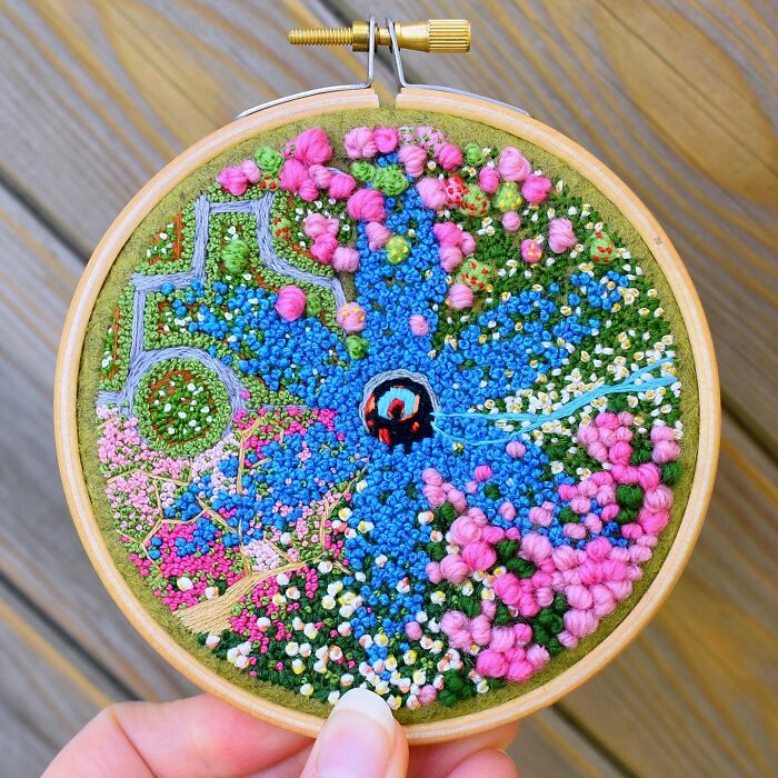 Colorful landscape embroidery art with blue and pink floral patterns in a wooden hoop.