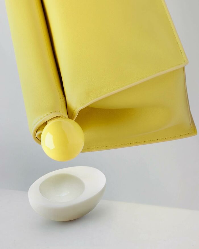 Yellow handbag resembling an egg yolk being c*****d into a white shell, showcasing illusion art fusion.