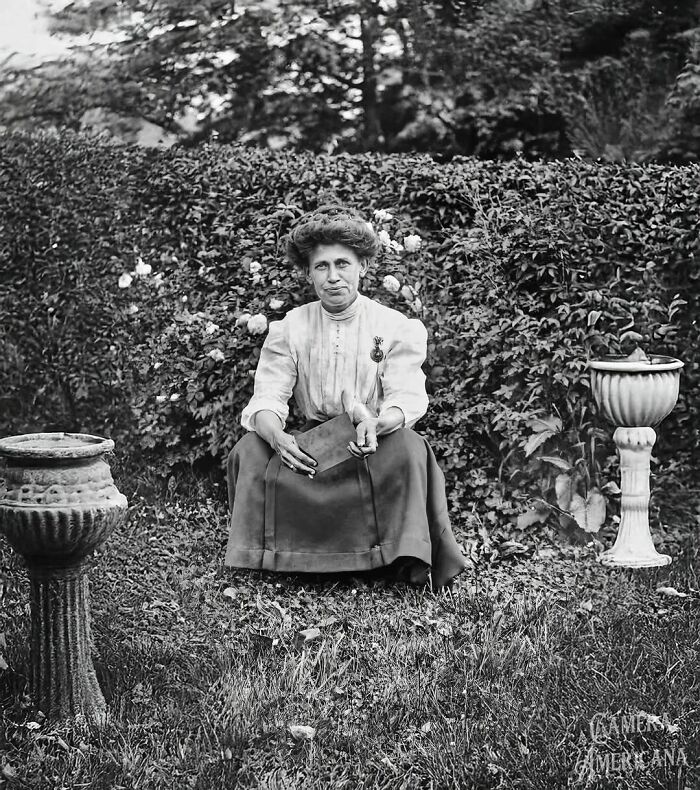 A woman in early 20th-century attire sits in a garden, capturing a lesser-known historical moment.