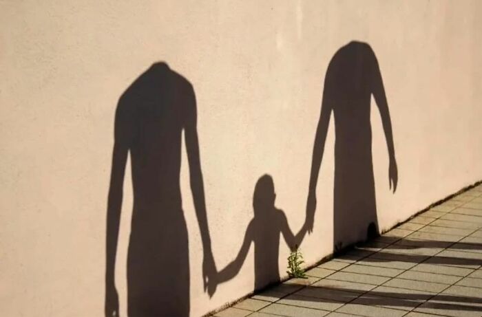 Shadows on a wall depict headless figures holding hands, creating a perfectly timed moment in street photography.