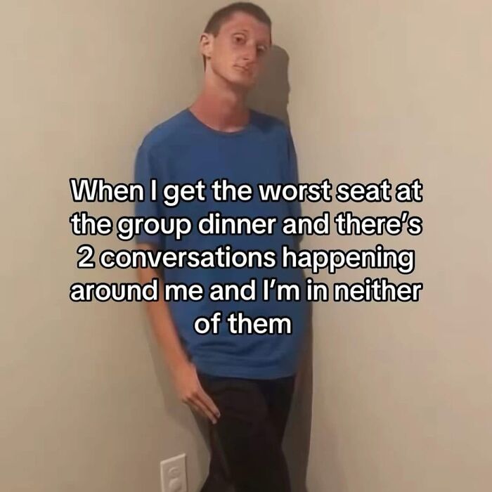 Man in blue shirt leaning against wall with funny meme text about awkward seating at group dinner.