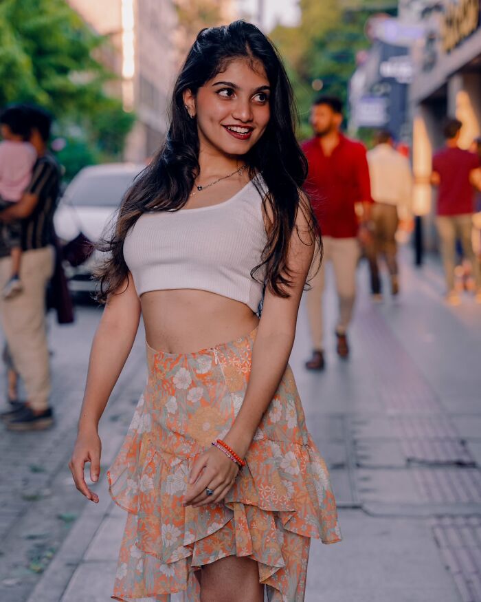 Indian photographer captures a smiling woman in a white top and floral skirt on a bustling street.