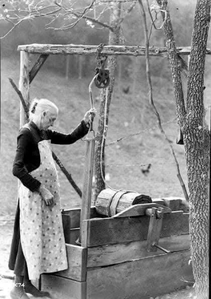 Elderly woman in an apron using a hand-cranked washing machine, evoking nostalgia with historical charm.