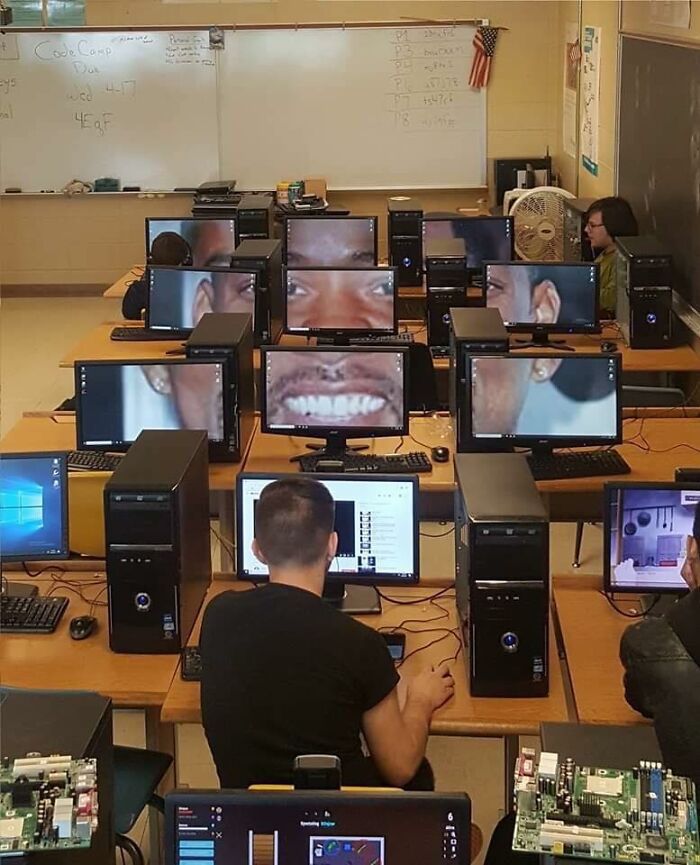 Classroom with multiple computer screens displaying a zoomed-in funny face, adding humor without context.