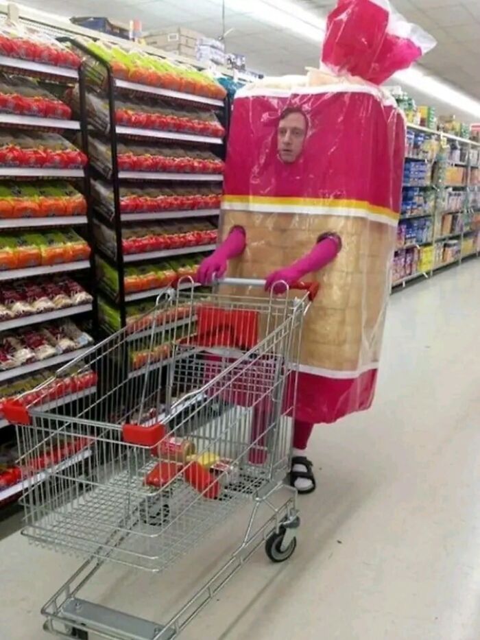 Person in a funny bread costume pushing a shopping cart in a grocery aisle.