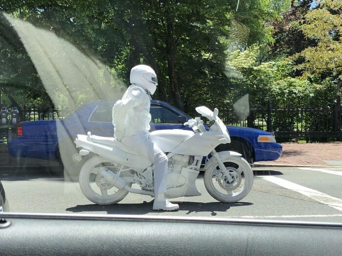 A person in all-white gear on a white motorcycle, creating a humorous scene at a traffic stop.