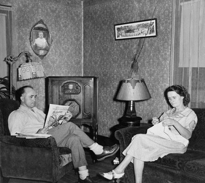 A couple in a vintage living room, man reading a newspaper, woman knitting, highlighting historical lifestyle moments.