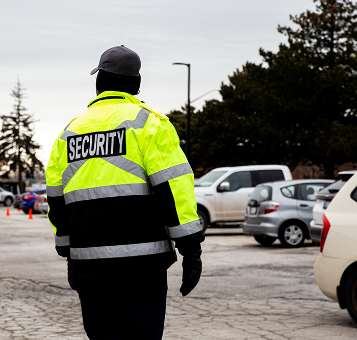 Security guard in a bright jacket, standing in a parking lot near a mall entrance. Security guard in a bright jacket, standing in a parking lot near a mall entrance.