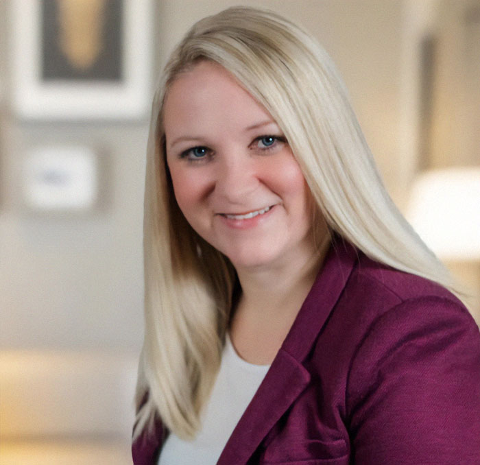 Blonde woman smiling, wearing a purple blazer, representing news on a woman's controversial restaurant bill incident.