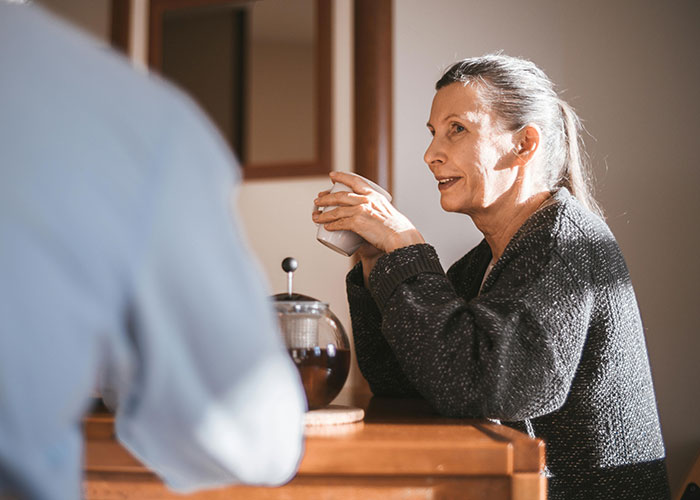 Woman smiling with a mug in hand, positive reaction during a conversation, related to coming out.