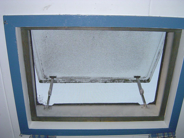 A blue-framed pop-out window viewed from below, featuring a clear glass pane slightly open to the sky.