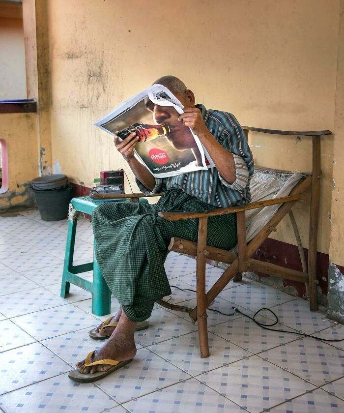 Man reading a magazine featuring a Coca-Cola ad, creating a perfectly timed street photo moment.