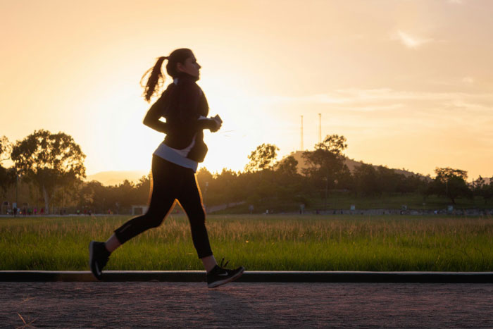 Woman running on a path at sunrise, engaging in a 5k run with trees and hills in the background.