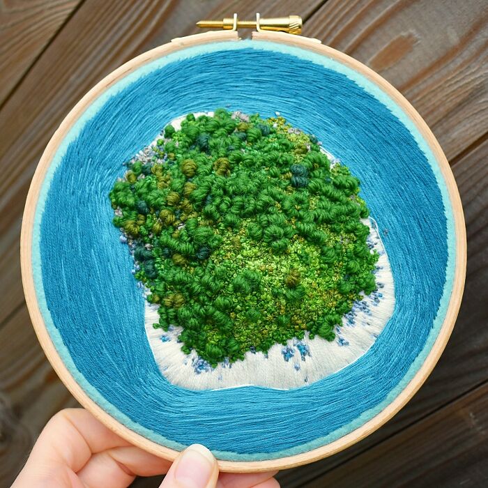 Landscape embroidery showcasing lush greenery and blue water in a circular hoop.