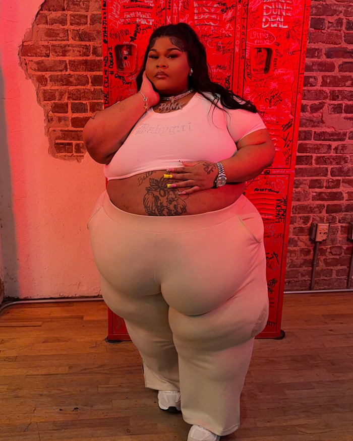 Rapper goes viral in stylish photoshoot, wearing white top and beige pants, standing by red graffiti wall. Rapper goes viral in stylish photoshoot, wearing white top and beige pants, standing by red graffiti wall.