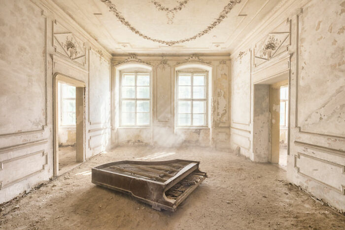 Abandoned place with decaying piano in a dusty, sunlit room.