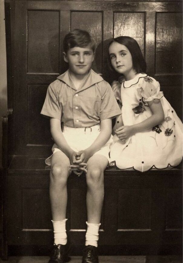 Vintage photo of a boy and girl sitting closely on a wooden bench, showcasing an interesting historical moment.