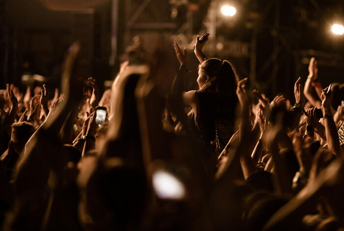 Crowd enjoying a live concert, people raising hands, capturing the moment with phones.