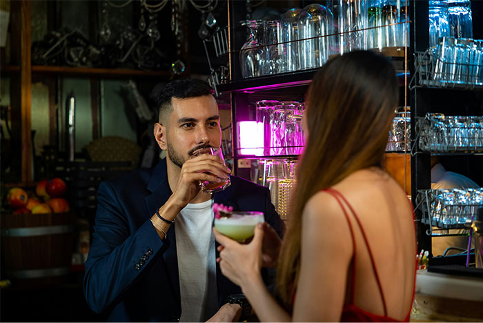 Man in a bar discusses solution for male loneliness with woman, holding drinks.